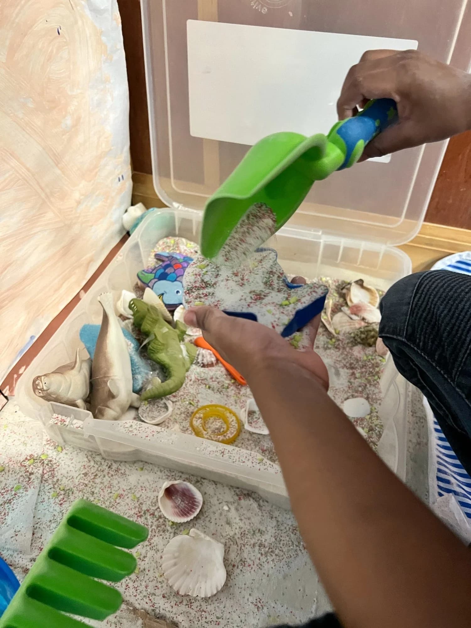 Close-up of a child exploring a sensory bin filled with sand, shells, and toys