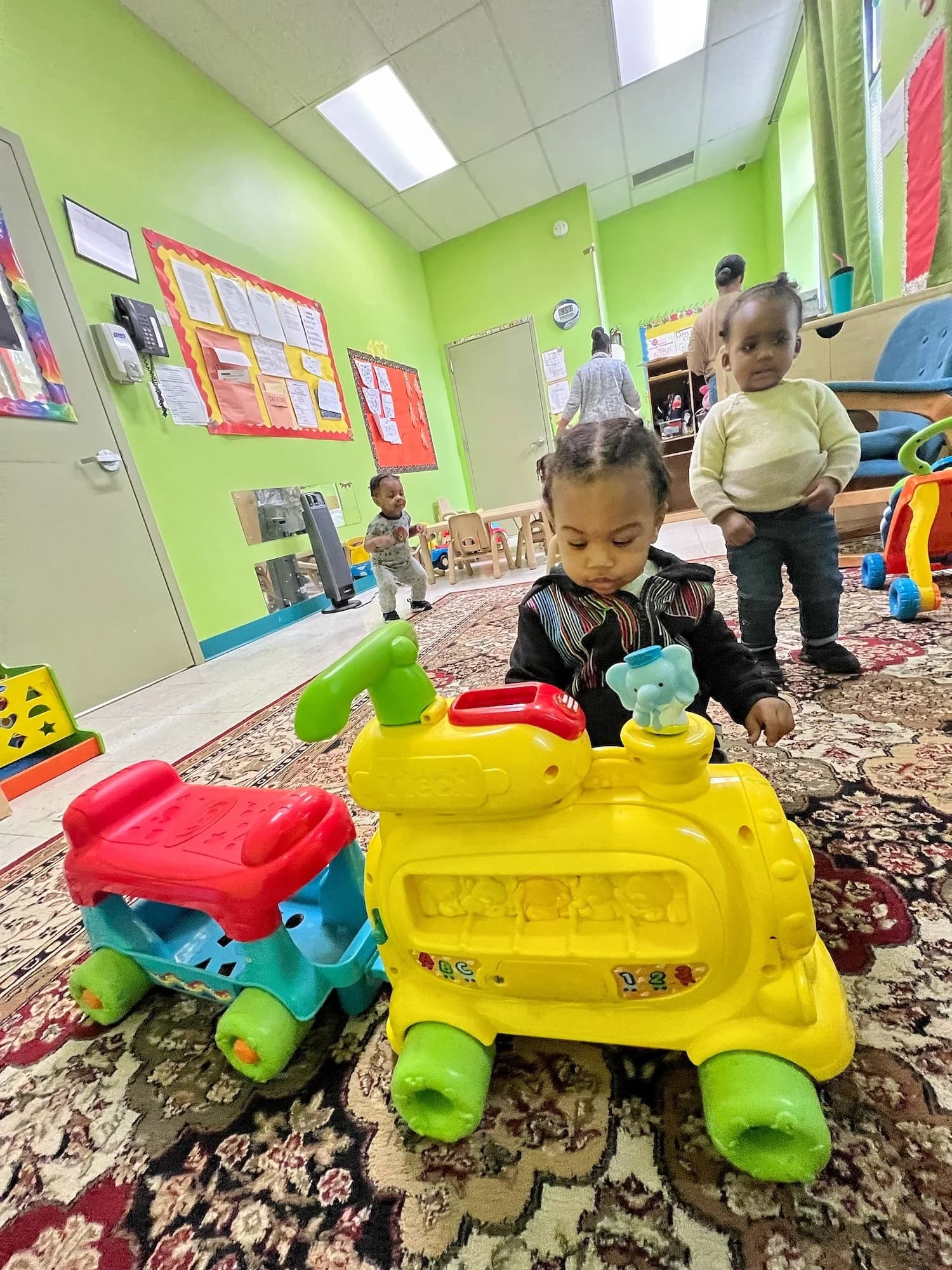 Toddlers playing with colorful toy trains in a bright classroom