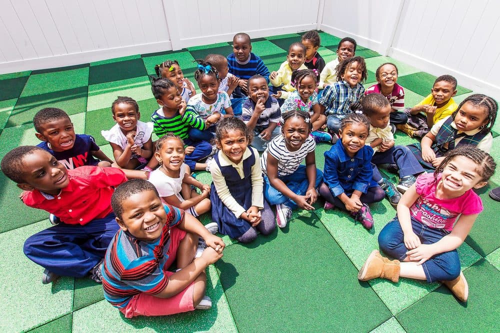 Children smiling and sitting together on the Einstein Daycare outdoor playground